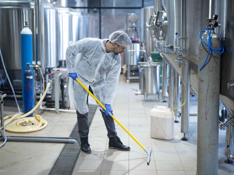 Professional industrial cleaner in protective uniform cleaning floor of food processing plant. Cleaning services.